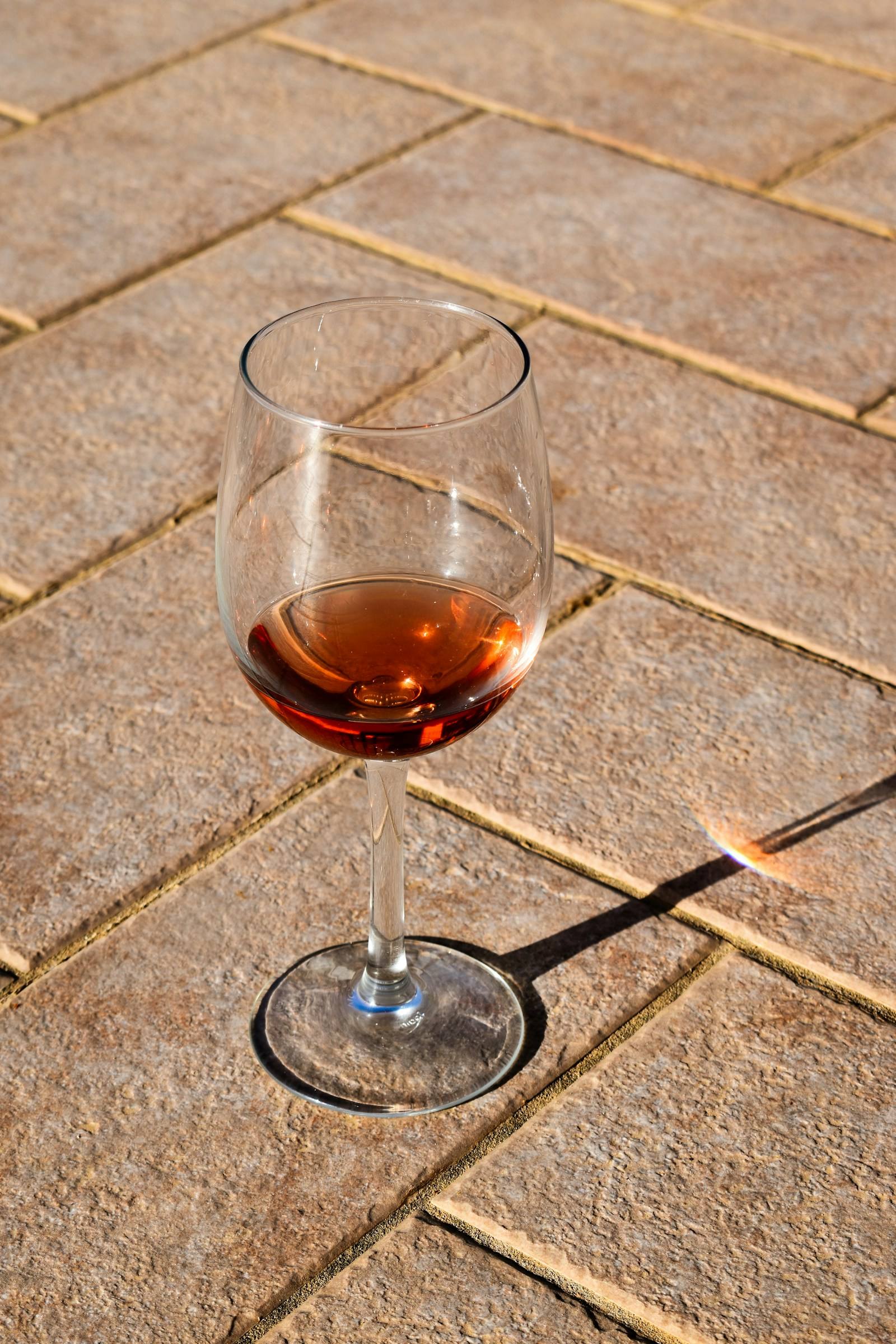 Ein Glas Bernsteinwein auf sonnigen Steinfliesen, mit langem Schatten
